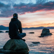 Silhouette of person sitting on rock looking out at sunset over water
